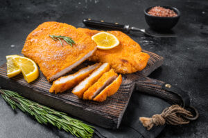 Fried sliced weiner schnitzel on a wooden board with herbs. Blac