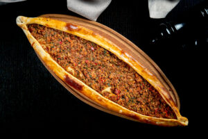 Turkish pide with minced lamb, tomatoes, bell pepper served on wooden tray. black background